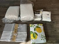 Photo showing white pillow covers and two rolls of white fabric/textile, striped grey and white place mats, and lemon print tablecloth.