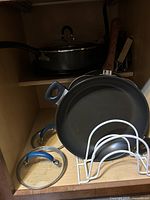 Cookware set including large frying pan with wooden handle, two glass lids with blue handles, and metal utensil rack.