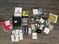 Overview photo showing the entire lot of Oakley tech accessories including phone cases, glasses, signs, and other small packaged items on wood floor.