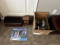 Overview photo showing the Expo marker set in packaging, the wooden organizer with metal dividers and drawer, and the cardboard box with assorted office supplies on the floor.