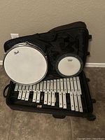 Photo showing the Pearl snare drum, Remo practice pad, glockenspiel, and mallets arranged inside the wheeled black case.