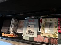 Top-down view of trunk showing various books, magazines, folded linens, and a decorative picture frame with frog design inside.