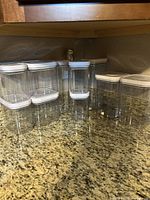 Ten clear plastic storage containers with white airtight lids arranged on a kitchen counter, showing variety of sizes.