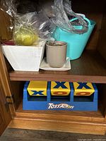 Shelf showing white square planter, beige honeycomb textured planter with saucer, turquoise bucket-style planter with handles, a bag with an unknown yellow item, and a Toss Across game below.