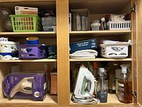 View of cabinet shelves showing cleaning baskets, iron and iron rest, and assorted cleaning supplies