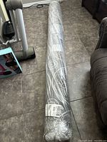Photo of rolled area rug on tiled floor, sealed in plastic wrapping, showing overall item condition and packaging.