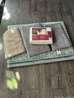 Green quilted cushion rug, beige cushioned rug pad, tan bath mat stacked and laid on floor