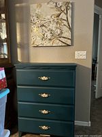 Full view of teal dresser with four drawers and gold ornate metal handles, canvas print hung above it