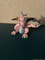 Front view of Coy Mood Dragon figurine showing pink porcelain with blue wings and belly, holding a small crystal in right hand.