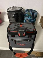 Full view of the Titan cooler in front of two packed sleeping bags, one black and one camouflage.