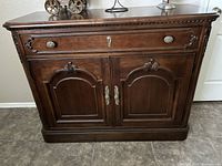 Front view of the wooden buffet cabinet showing the drawer and two cabinet doors with decorative metal handles and carved detail.