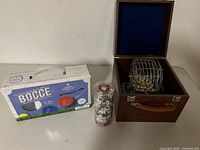 Full view of unopened bocce set box, dice container, and bingo cage in wooden box