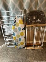 Photo showing metal drying rack, folded ironing board with patterned cover, and folded laundry bag with wooden frame