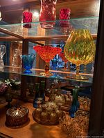 Shelf with multicolored vintage glass vases and bowls including red vase, yellow vase, blue bowl