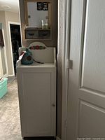 White wooden storage cabinet with a floral decoration on the top back panel and its contents on top and inside.