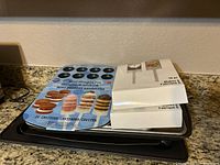 Photo shows Wilton Mini Whoopie Pie pan with blue cardboard backing advertising 24 cavities, and stacked metal cookie and muffin pans underneath on kitchen countertop.
