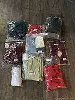 Nine assorted packages of new women's clothing laid out on floor showing variety of colors and items.