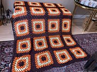 Full view of the hand crocheted afghan draped over a surface showing the square pattern and colors.