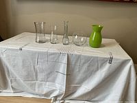 Five glass vases of assorted shapes displayed on a white cloth-covered surface