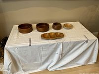 Front view of the assortment of wooden bowls and compartment dish on a white cloth-covered table.