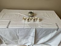 View of Bulgarian pottery set with six small tumblers and decorative pottery bowl on a white embroidered tablecloth.