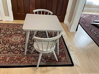 Photo of the small square table with two spindle-back chairs on a patterned rug showing overall set.