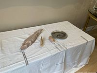 Image showing three colored stone animal decorations (crocodile, fish, hippopotamus) and a silvered hanging plate placed on a white embroidered cloth.