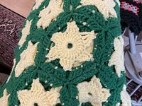 Close-up of a section of the afghan showing the hand crocheted gold star/flower pattern within green squares and thick yarn texture.