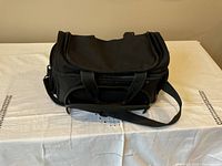 Front and top view of black insulated travel bag, showing handles and shoulder strap on white cloth surface.