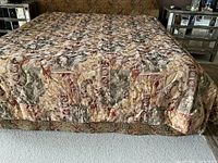 Full view of the king size bed with quilted duvet cover showing multicolor floral and ornate pattern on bed spread and shams, bed skirt visible underneath.