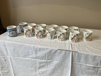 Eleven mugs arranged on white cloth, showing winter and Snowman artwork
