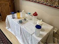 Eight assorted travel bottles arranged on white tablecloth, variety of sizes and caps, clear and colored plastic bottles visible.