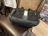 Front view of Travelpro bag showing external zippered pocket and ID holder on black nylon material.