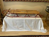 Side profile of vintage wooden and metal sleigh showing wooden seat slats and red metal frame with curved front handles.