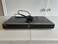 Front and top view of a black Sharp Blu-Ray Disc Player BD-HP22U with power cord coiled on top.