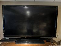 Front view of Sharp Aquos TV with stand, remote, and power cable