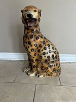 Front view of the ceramic leopard figurine sitting on tiled floor against wall.