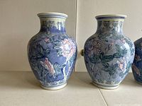 Front view showing two taller vases with blue background and pink floral designs, white rims with blue detailing