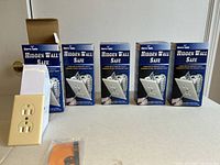 Five boxed Sierra Tools Hidden Wall Safes displayed with one safe removed from box showing beige electrical outlet style design.