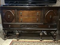 Wooden hutch showing front view with ornate carved panels, metal handles, and turned legs.