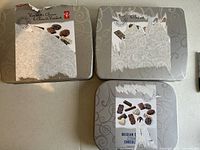 Top view of three rectangular metal tins showing partial paper labels with Belgian chocolate imagery and text, some paper ripped off.