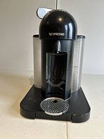 Front angle view of black Nespresso coffee machine showing nozzle, water reservoir and drip tray.