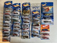 Overall view of more than 30 Hot Wheels cars in original packaging, arrayed on table showing different colors, models, and series.
