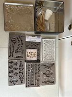 Photo of rectangular embossed metal storage tin with lid slightly off showing inside contents and silicone moulds spread in front