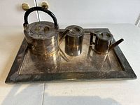 Silver plated tea set with teapot, creamer, sugar bowl, and tray, viewed from a slight angle showing tarnish needing cleaning.