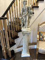 Full view of the statue on the column stand showing placement and proportions next to a staircase and ornate chair.