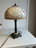 Full view of the Tiffany style table lamp showing the ornate base and dome-shaped shade with colorful floral patterns.
