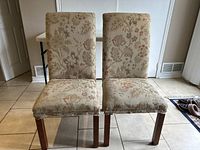 Two upholstered dining chairs with floral-patterned fabric and wooden legs, showing front view.