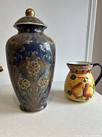 Photo of decorative ceramic vase and water pitcher showing detailed floral and pear designs.