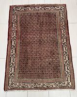 Full view of rectangular hand-knotted Arak Persian rug showing brown background with repeating small motifs and beige border with geometric pattern.